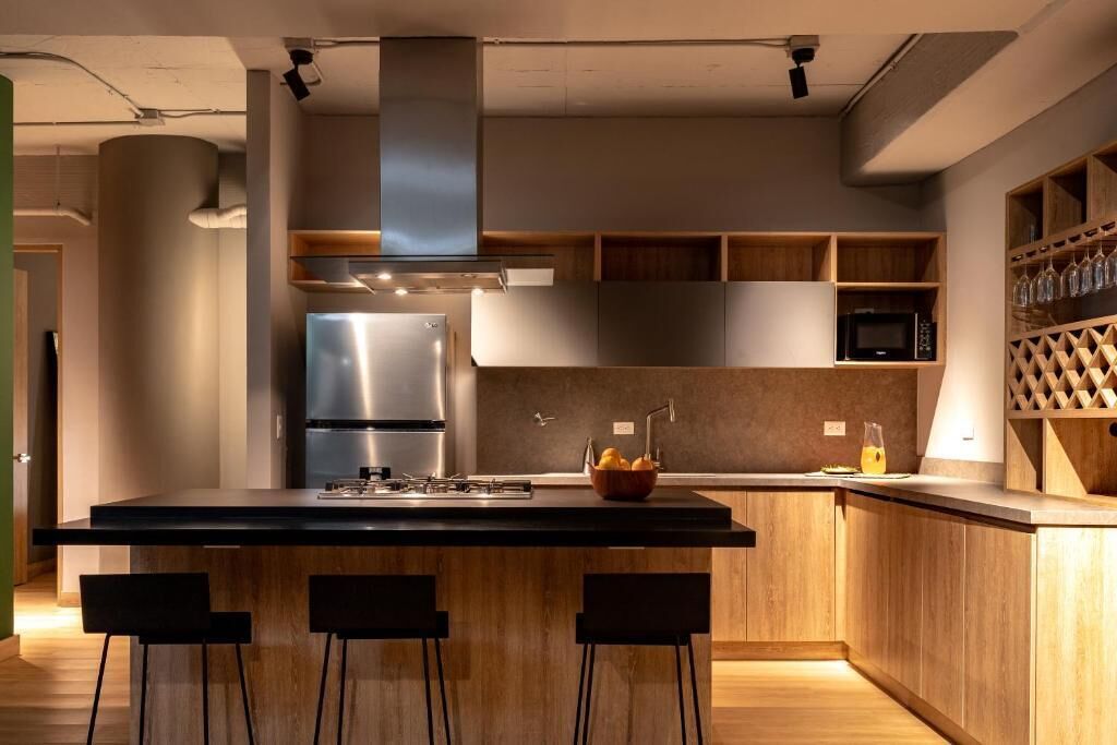 A modern kitchen with a central island, bar stools, stainless steel appliances, wooden cabinetry, and a wine rack.