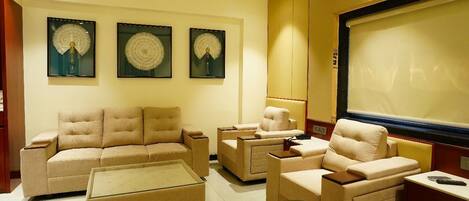Una sala de estar moderna con un sofá color beige, una mesa de centro de vidrio y un televisor de pantalla plana. Tres obras de arte enmarcadas decoran la pared sobre el sofá.