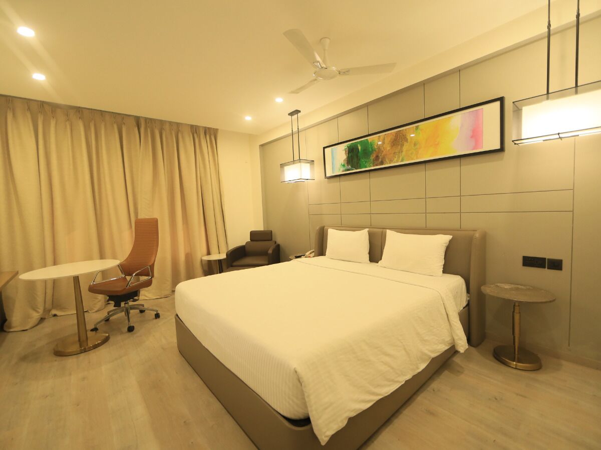 A hotel room with a large bed, a desk, a chair, and a small table.