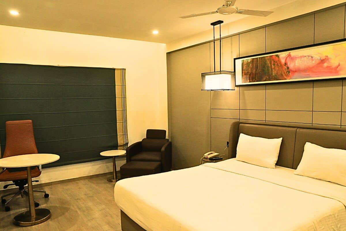 A hotel room with a large bed, a desk, a chair, and a painting on the wall.