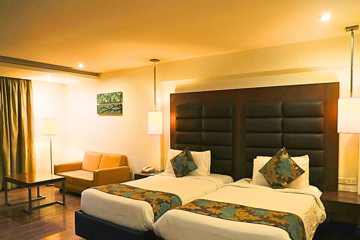 A hotel room with two beds, a sofa, a desk, and a lamp.