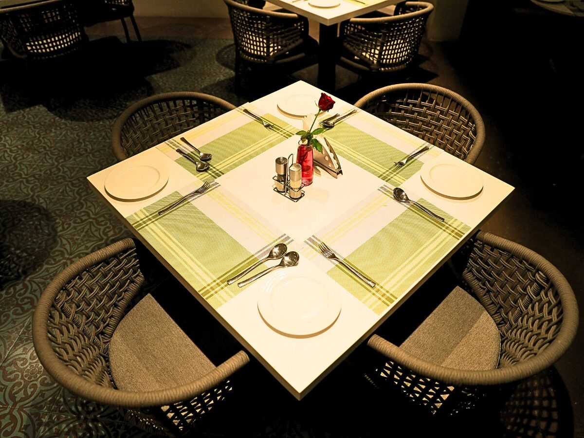 A square dining table with a green and white checkered tablecloth, surrounded by four wicker chairs.