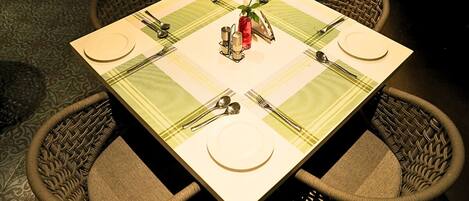 Una mesa cuadrada para comer con mantel a cuadros verdes y blancos, rodeada por cuatro sillas de mimbre.