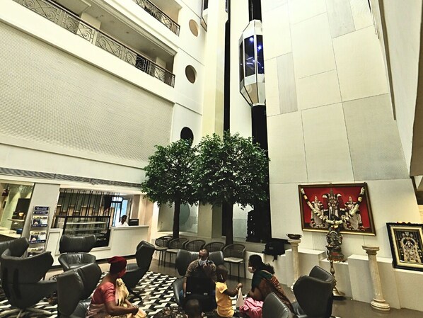 A lobby with a reception desk, seating area, and a large artificial tree. - D.R Utthama Nellore AM Hotel Kollection (Nellore)