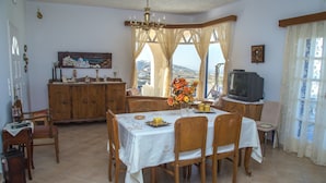 A dining area with a table set for four, a wooden cabinet, a television, and a view of the outdoors. - Villa Eva with Panoramic view (Santorini)