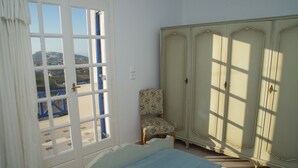 A room with a bed, a chair, a wardrobe, and a window with a view of a landscape. - Villa Eva with Panoramic view (Santorini)