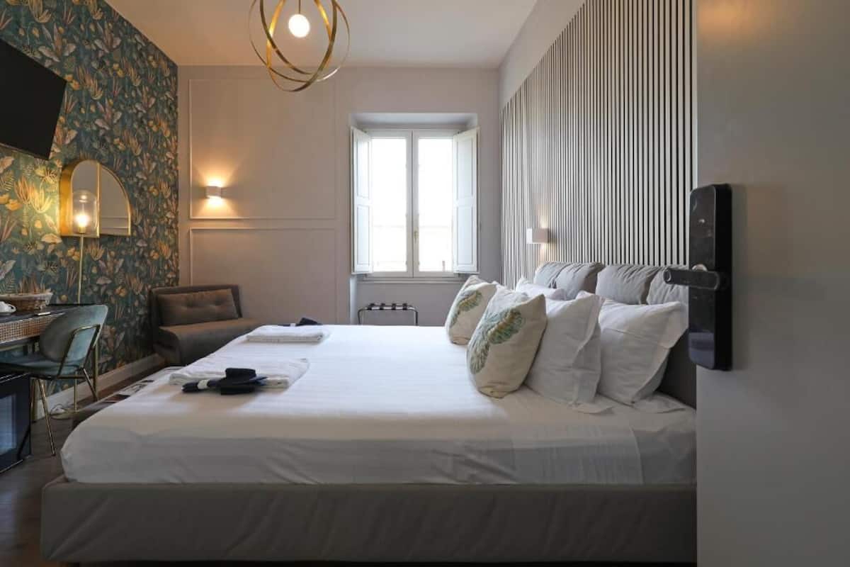 A neatly arranged hotel room with a large bed, a desk with a chair, a window with curtains, and a wall-mounted TV.
