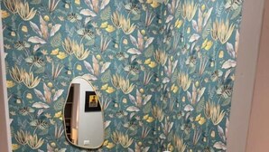 A room with a blue sofa, a round side table with a lamp, and a wall with a leafy pattern. - Plaza Suites Rome (Rome)