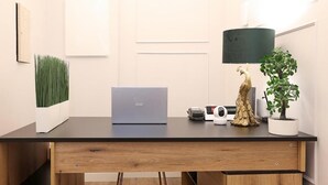 A modern office desk with a laptop, a plant, a decorative tree trunk, and a lamp. - Plaza Suites Rome (Rome)