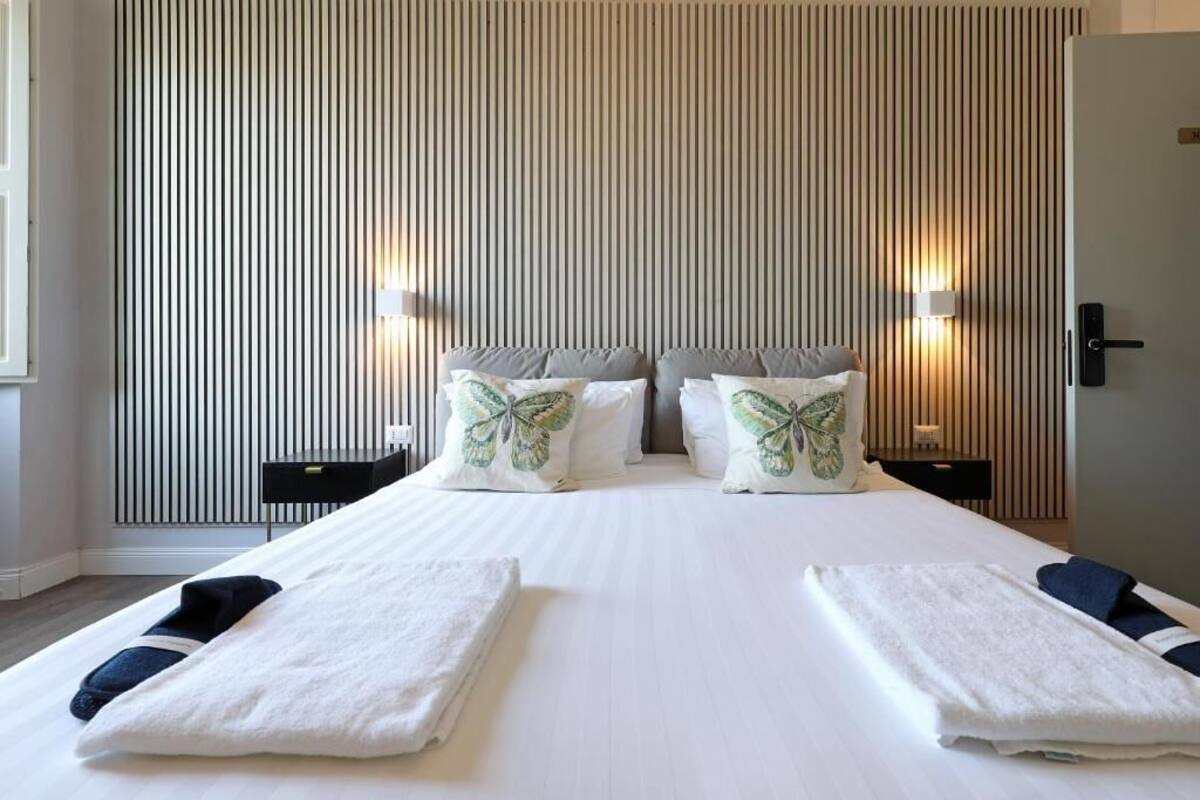 A hotel room with a large bed, two bedside tables, and a wall with vertical blinds.