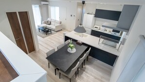 A modern kitchen with a dining table, chairs, and a pendant light. - Mova Villa Okino (Kikuyo)
