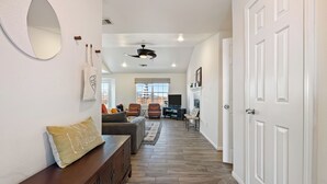 A spacious living area with a sofa, a coffee table, and a fireplace. There is a large mirror on the wall and a ceiling fan.