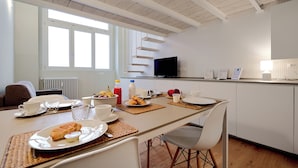A modern kitchen with a dining area, featuring a long table with breakfast items, a television, and a window with blinds. - MILAN design Loft in great location (Milan)