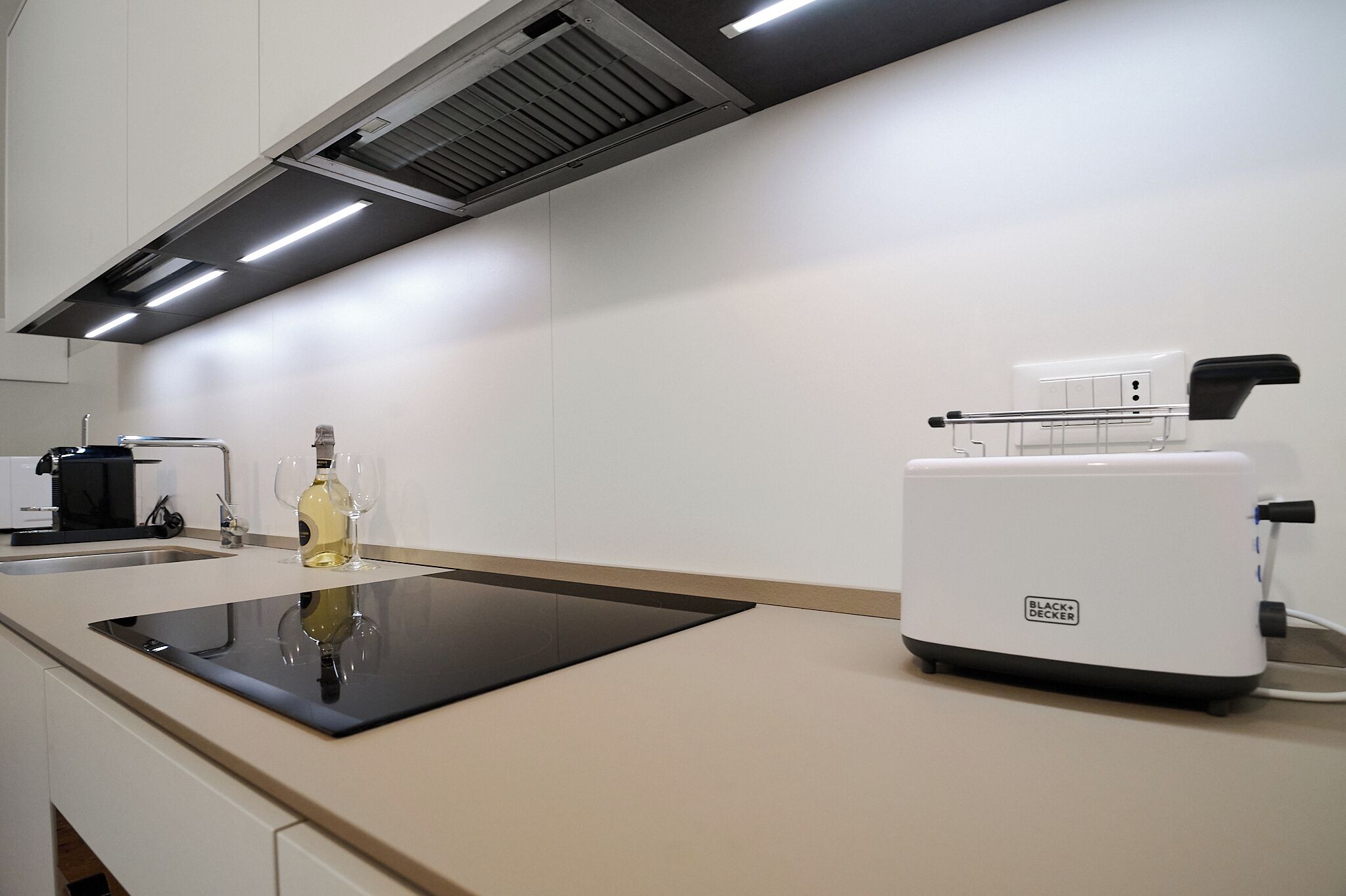 Une cuisine moderne avec une plaque de cuisson à induction noire, un grille-pain et une bouteille de vin posée sur le plan de travail.
