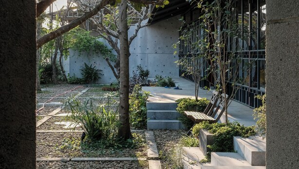 A courtyard with a pathway, trees, and a building with a glass facade. - De Hué Space (Hue)