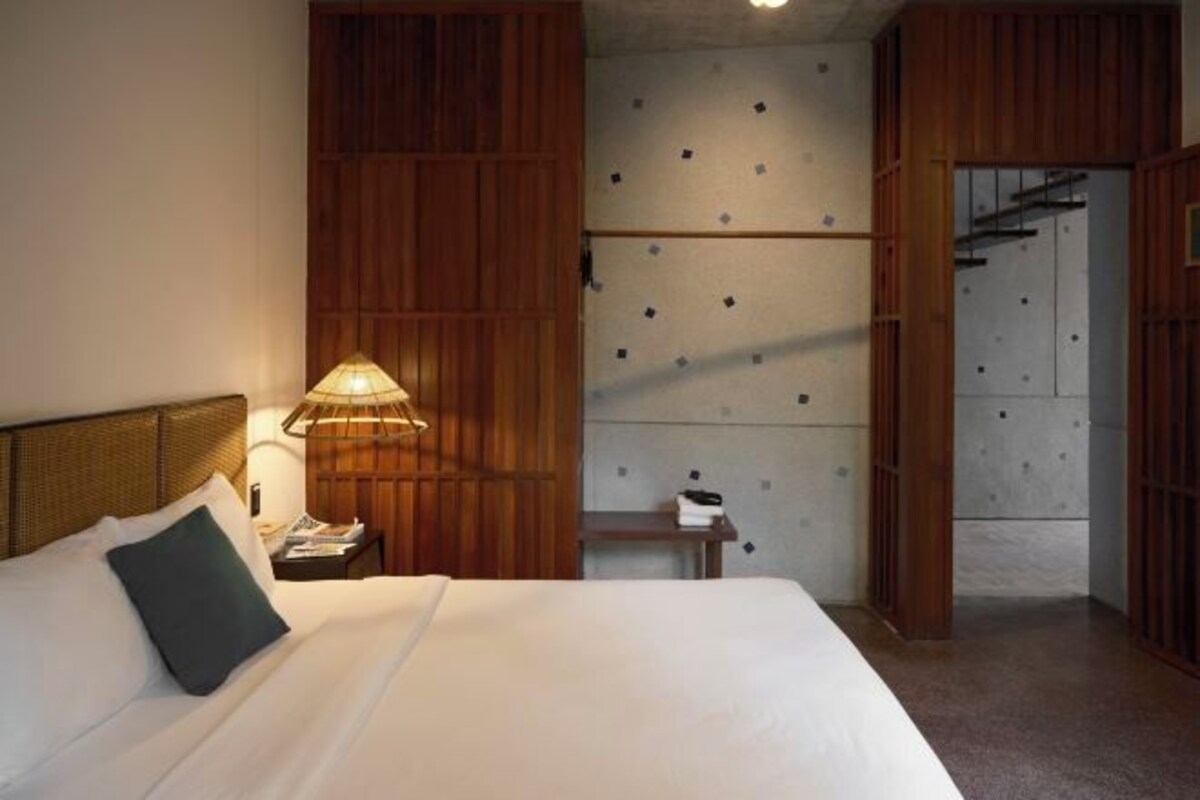 A hotel room with a bed, a nightstand, a lamp, wooden paneling, and a wardrobe.