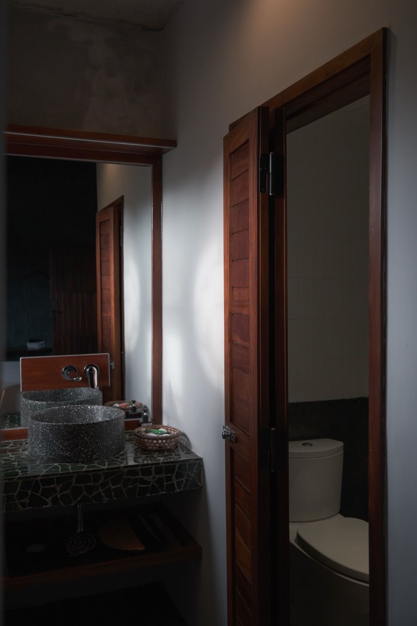 A bathroom with a wooden door, a sink with a stone countertop, and a toilet visible through the door.