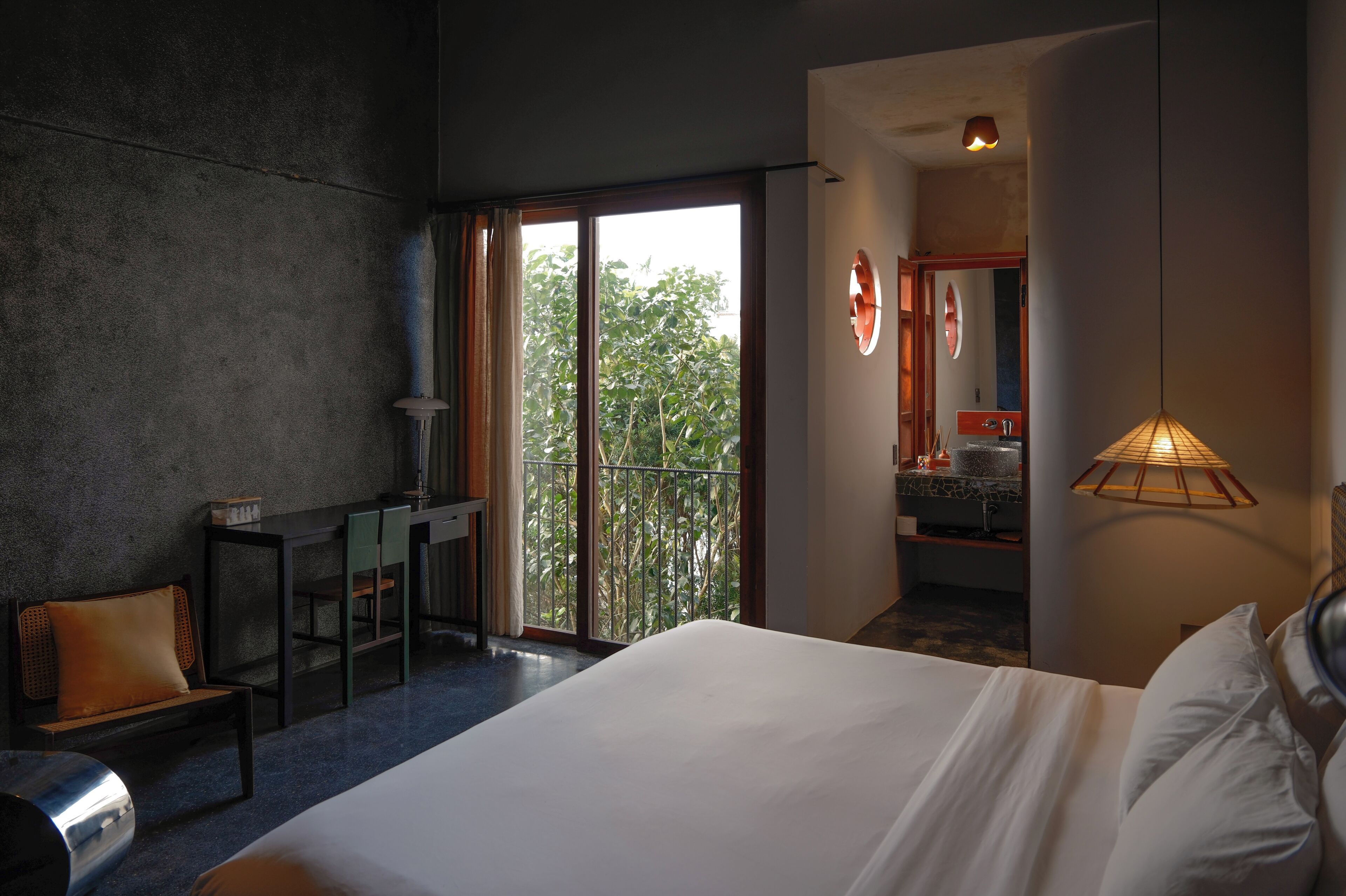 Ein modernes Hotelzimmer mit einem großen Bett, einem Schreibtisch und Blick auf einen Balkon mit Grünpflanzen.