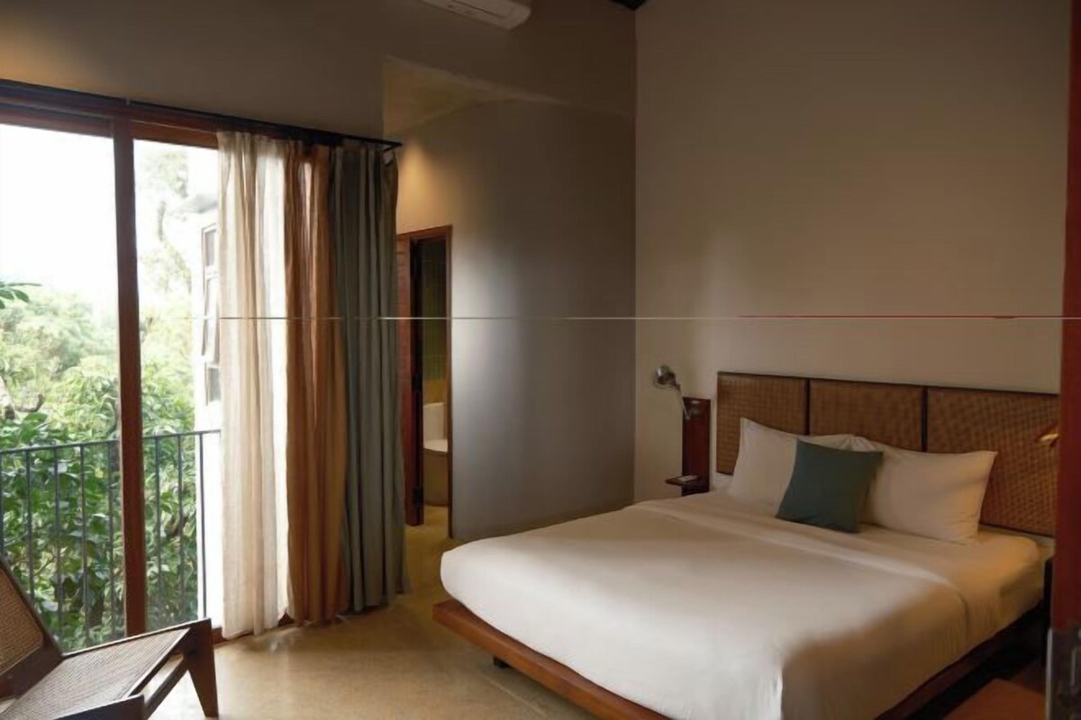 A hotel room with a bed, a chair, and a balcony with curtains.