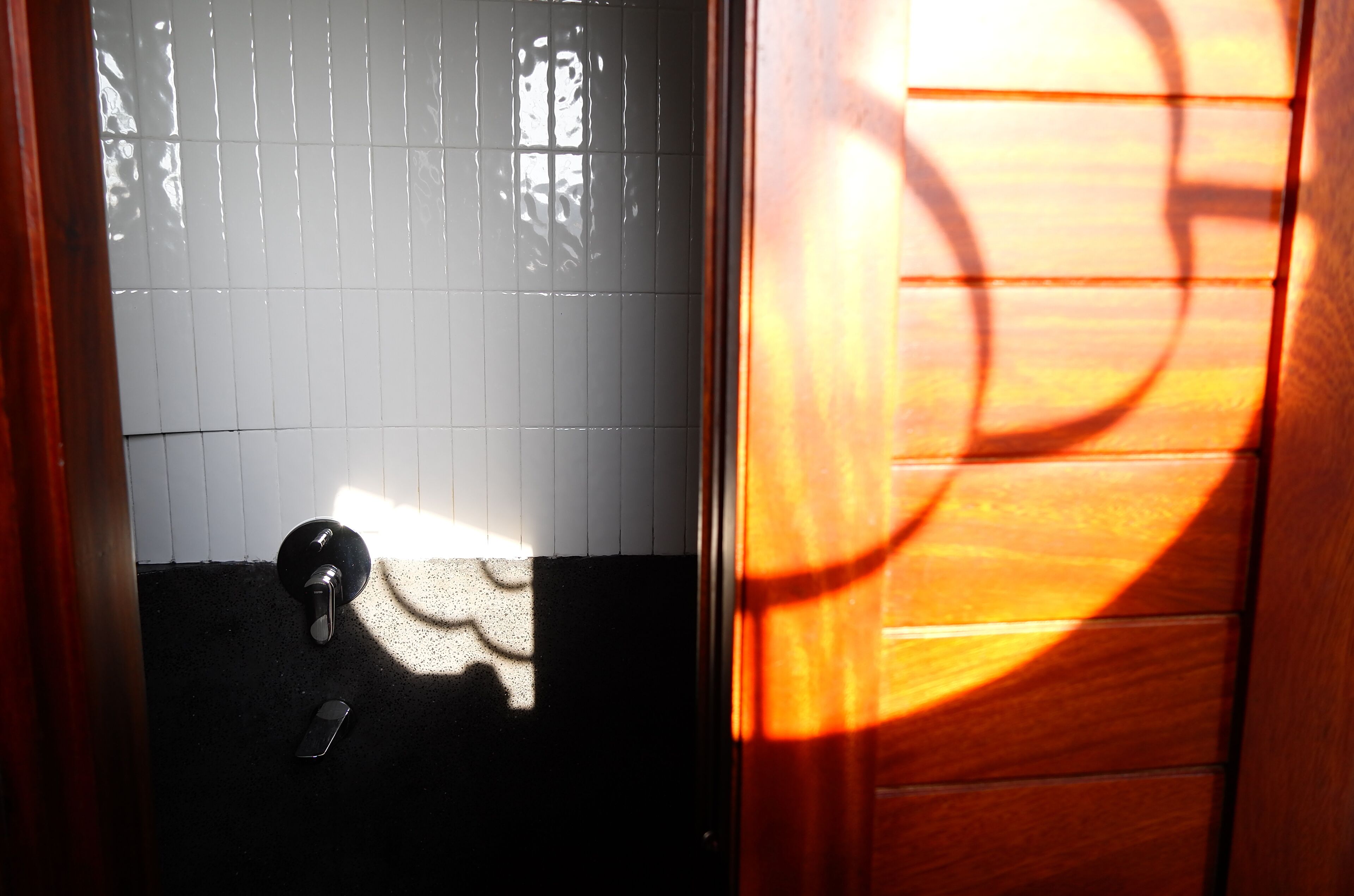 Una puerta con una cerradura y un tirador, un muro de azulejos y la sombra de un objeto circular.