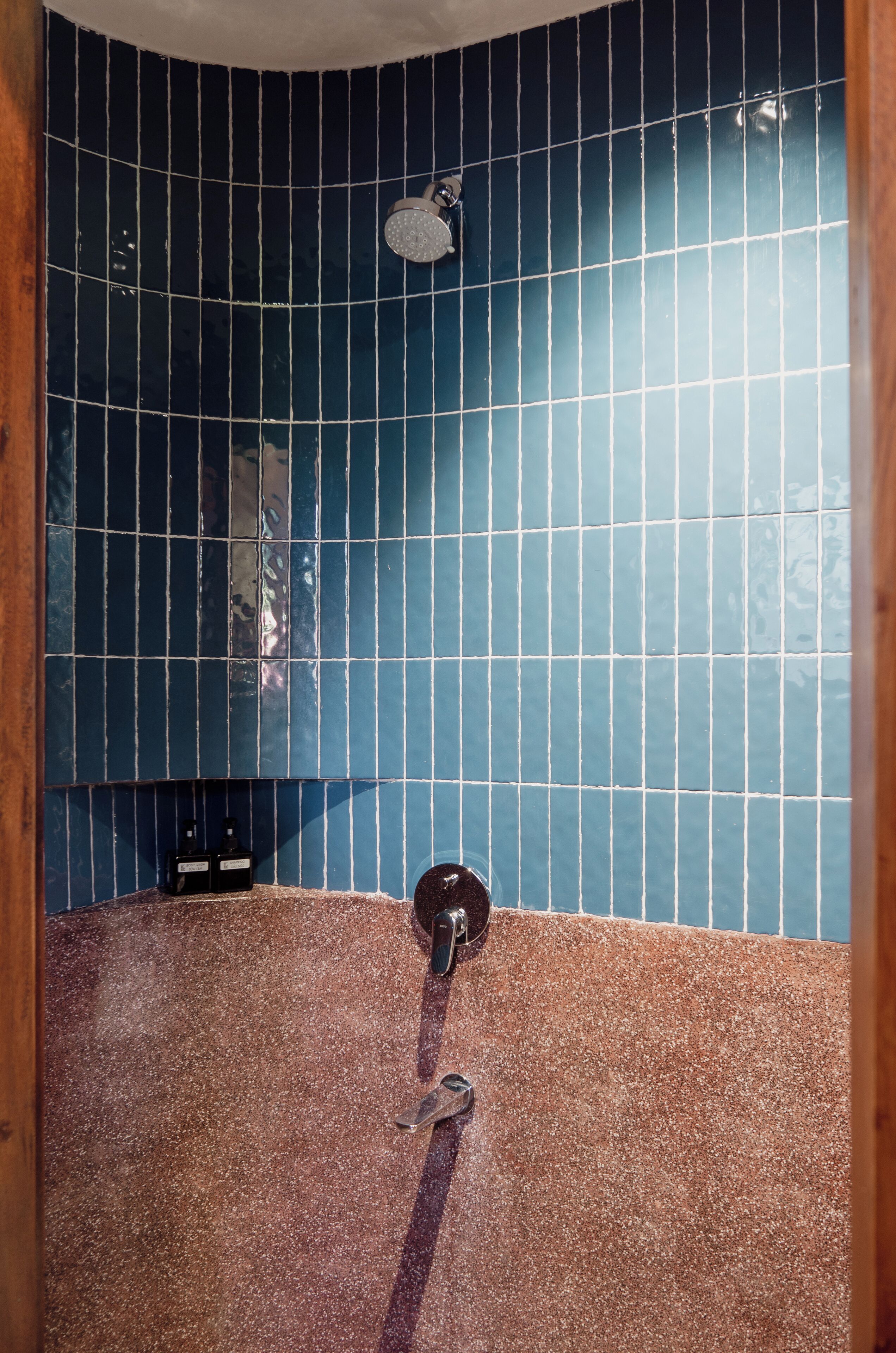 A bathroom with blue tiled walls, a showerhead, and a towel rack.