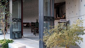A modern building with large glass doors, a staircase, and a small tree in a planter. - De Hué Space (Hue)