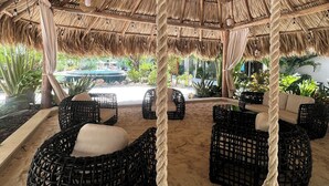 A thatched-roof outdoor seating area with wicker furniture and rope swings.