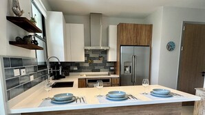 A modern kitchen with a central island, bar stools, a refrigerator, and a clock on the wall.