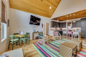 A spacious living area with a wooden ceiling, a dining set, and a kitchen area with modern appliances.