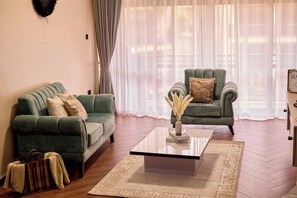 Una sala de estar con dos sofás verdes, una mesa de centro de cristal y una alfombra beige.