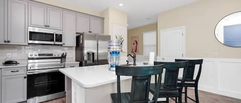 A modern kitchen with built-in appliances, a central island with bar stools, and a large mirror on the wall.