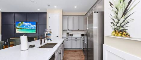 Una cocina moderna con armarios blancos, una isla grande con un lavamanos y un televisor de pantalla plana montado en la pared.