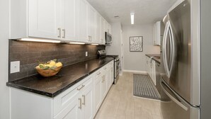 Una cocina moderna con armarios blancos, un refrigerador de acero inoxidable y un microondas.