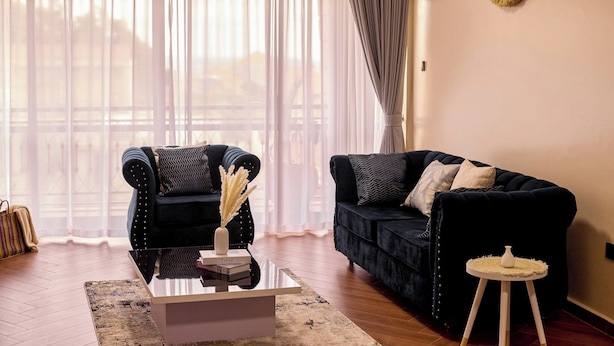 Un salon moderne avec deux canapés sombres, une table basse en verre et une petite table d’appoint.