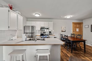 A modern kitchen with white cabinetry, a central island, and a dining area with wooden chairs. - Ski In/Out-3 Hot Tubs, Sauna, Gym, Mountain Views (Steamboat Springs)