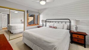 A bedroom with a large bed, a ceiling fan, a mirror, and a nightstand with a lamp. - Hike In/Hike Out w/Slope Views + 3 Hot Tubs-Ski/Town Shuttle-Sauna-Gym-Gas Fireplace-Deck-Updated (Steamboat Springs)