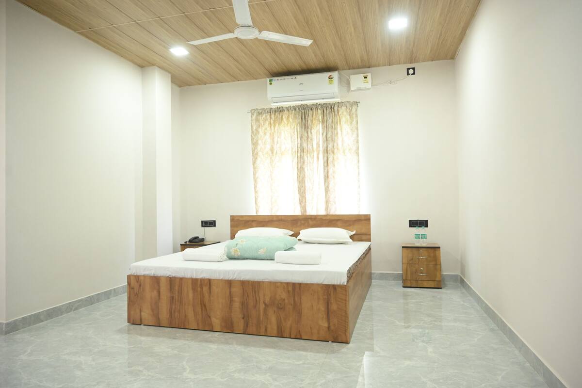 Une chambre à coucher avec un lit en bois, une table de chevet, une petite armoire en bois et un ventilateur de plafond.