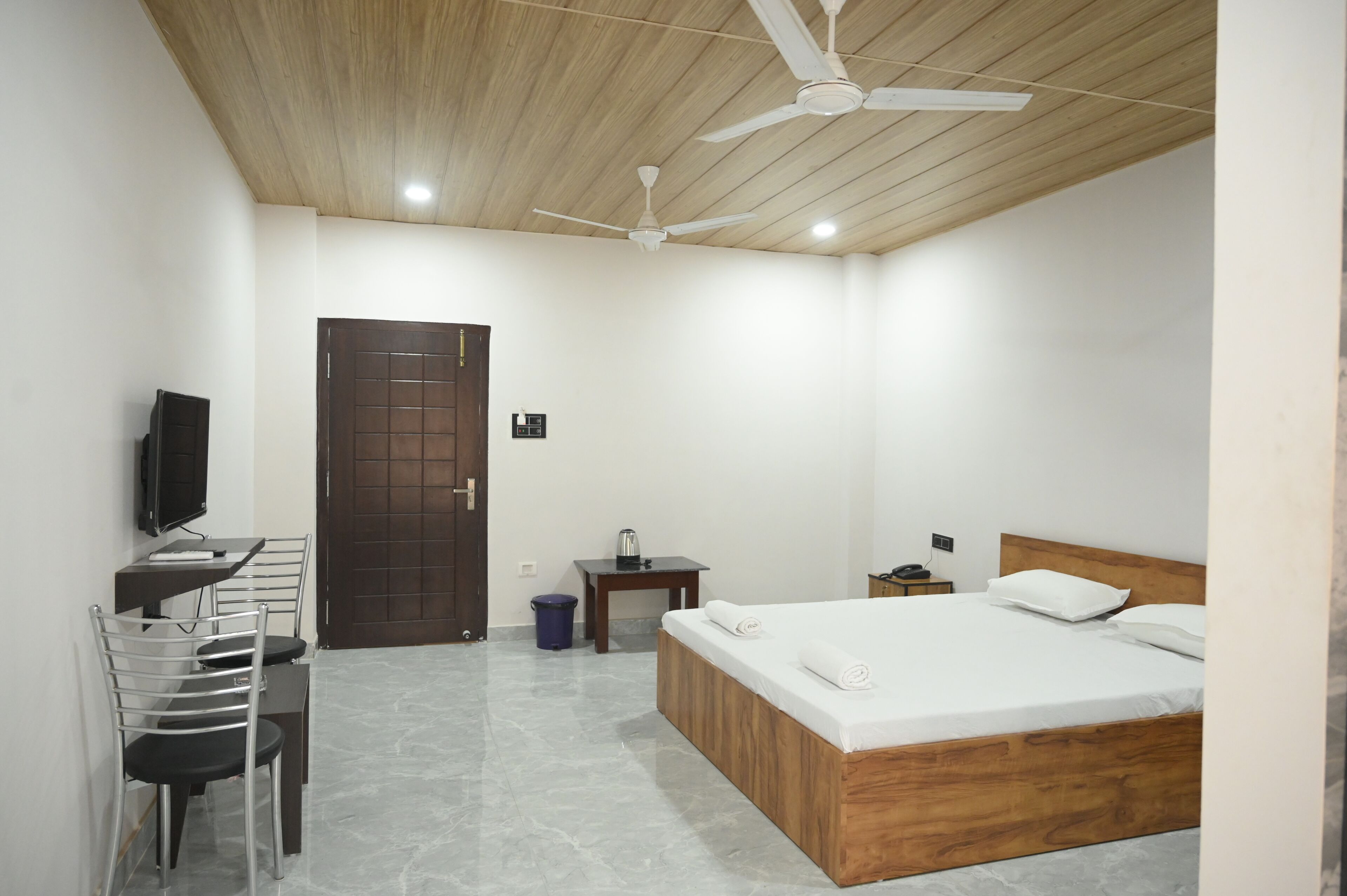 A bedroom with a wooden bed, a desk with a chair, a television, and a ceiling fan.