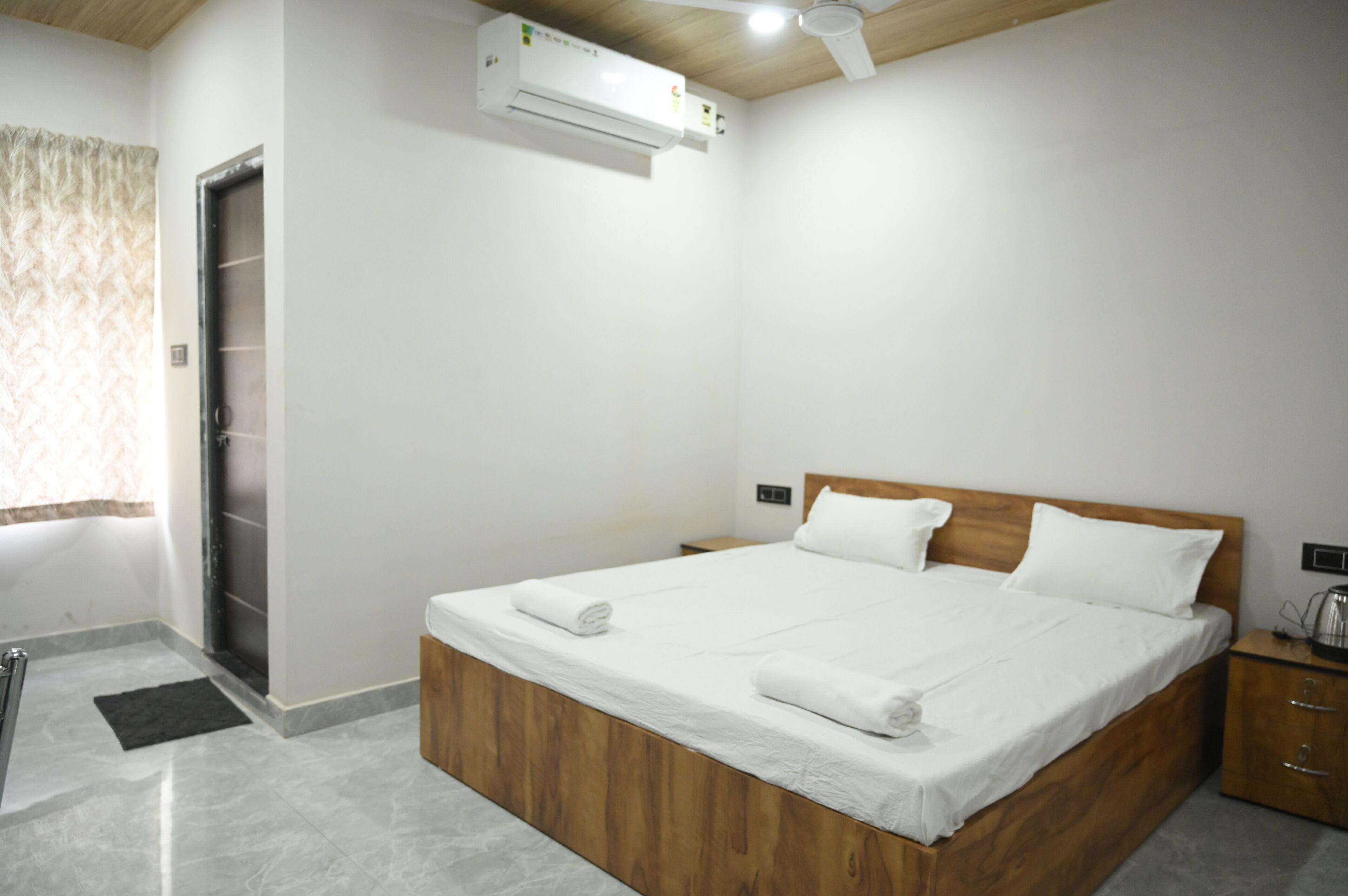 A bedroom with a wooden bed, white linens, a ceiling fan, and an air conditioning unit.