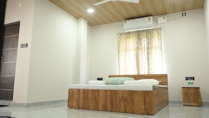 Quarto moderno com cama de madeira, ventilador de teto, ar condicionado e uma pequena mesa de cabeceira.