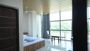 A modern bedroom with a wooden ceiling, a large window with curtains, a bed, a table, and a chair.