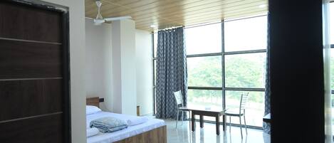 A modern bedroom with a wooden ceiling, a large window with curtains, a bed, a table, and a chair.