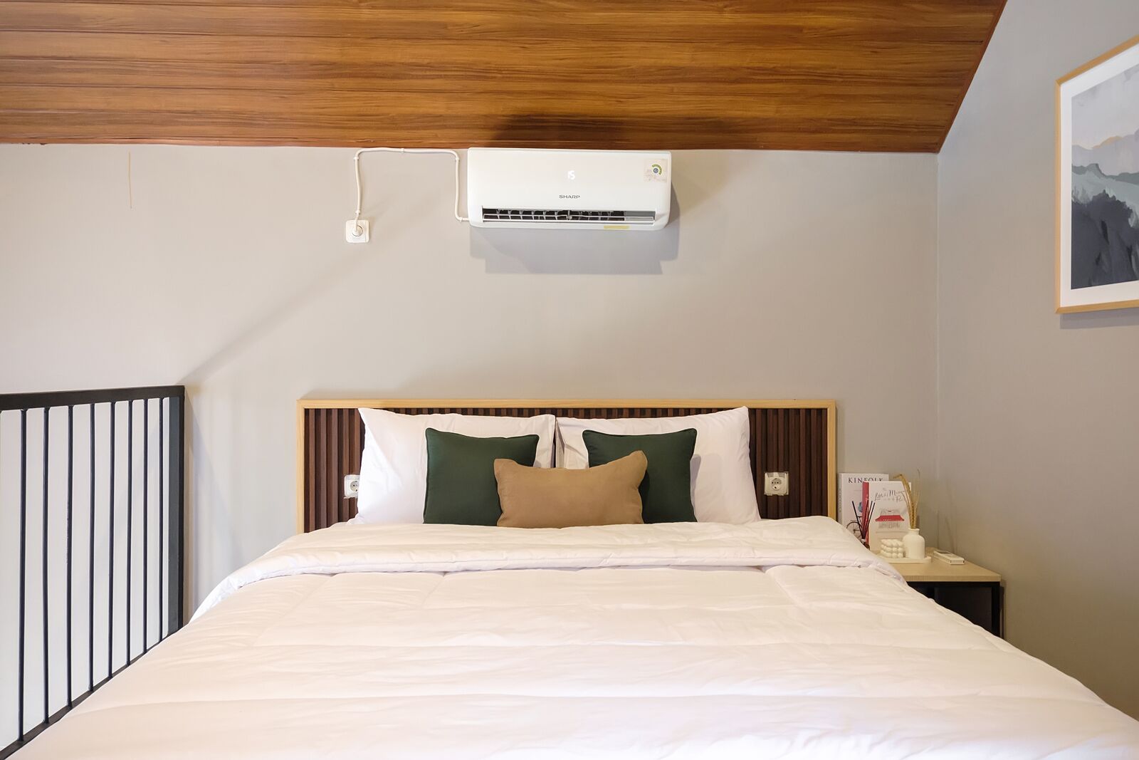 A hotel room with a bed, a nightstand, an air conditioning unit, and a framed picture on the wall.