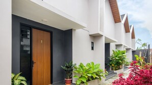 Un edificio moderno con puerta de madera, plantas en macetas y fachada blanca y cuidada.