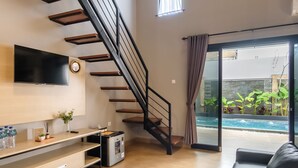 Una sala de estar moderna con una escalera, un televisor de pantalla plana, una cafetera y vistas a una piscina.