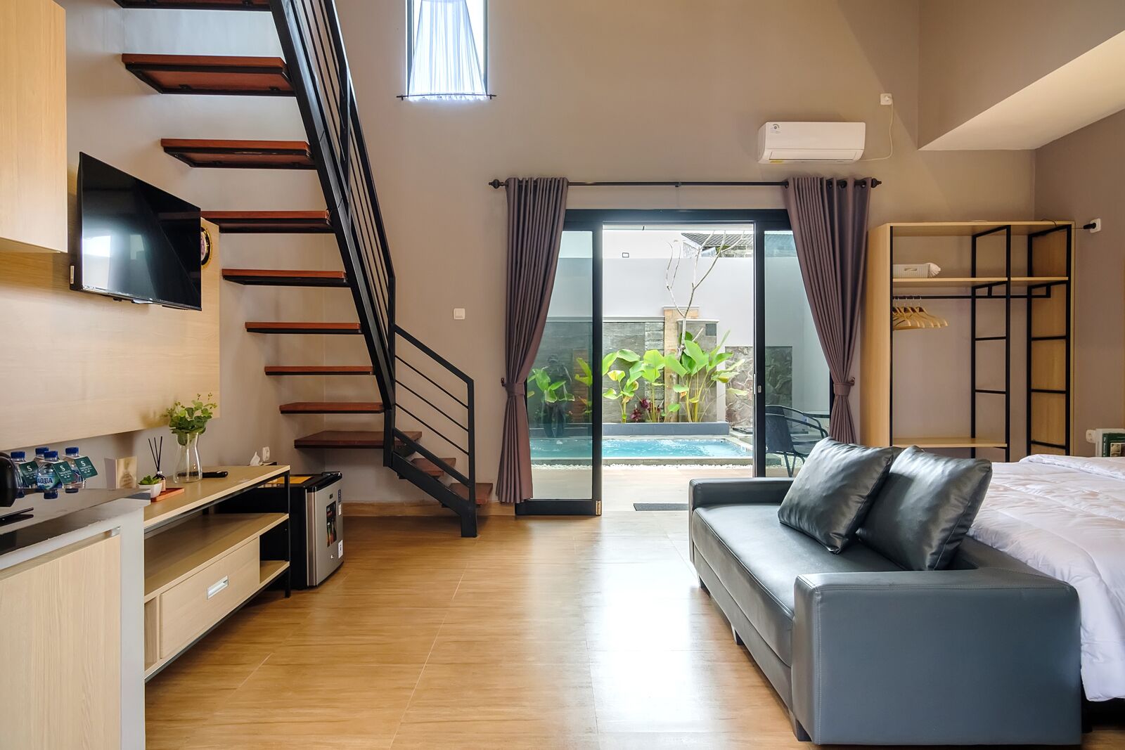 A modern hotel room with a staircase, a sofa, a TV, a desk, and a view of an outdoor pool.