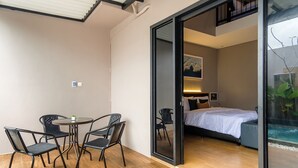 Una habitación moderna con cama, una pequeña mesa con sillas y un vidrio que da a un balcón con vistas a un jardín acuático.