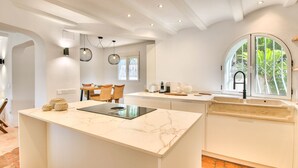 A modern kitchen with a marble countertop, a built-in island, and a large window with a view of greenery. - Luxury villa with sauna and private pool in Denia 10P (Denia)