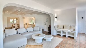 A modern living room with a sectional sofa, two round coffee tables, a built-in bench with cushions, and a dining area with a table and chairs. - Luxury villa with sauna and private pool in Denia 10P (Denia)