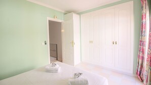 Quarto com cama, guarda-roupa e banheiro visível por uma porta aberta.
